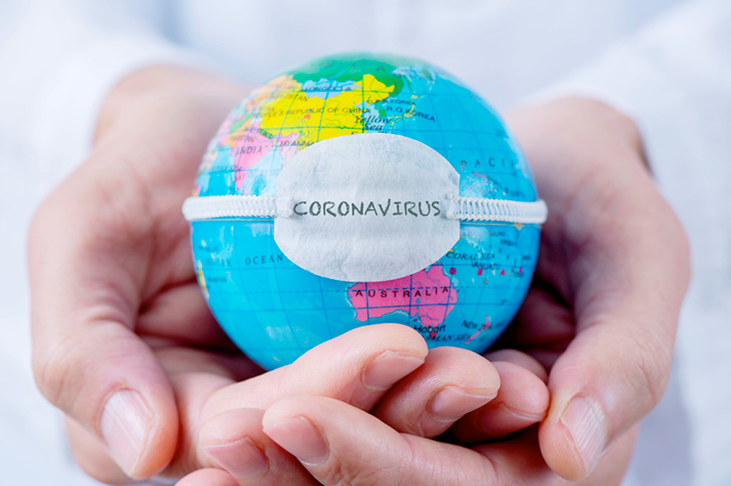 Cupped hands in foreground holding miniature globe wearing a 'Coronavirus' mask