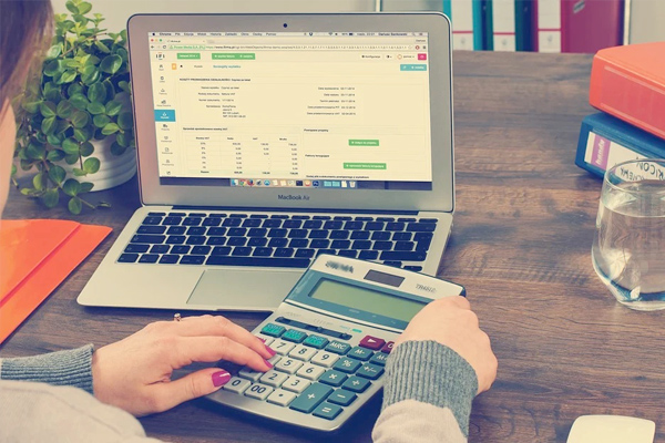 person with calculator looking at finanicals on a laptop