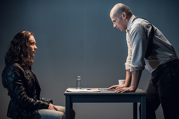 LSBME - investigator leaning over desk interrogating a seated person