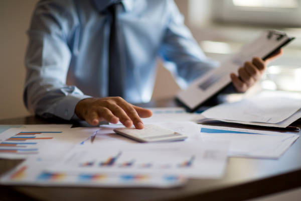 Businessperson evaluating numbers at desk cluttered with charts
