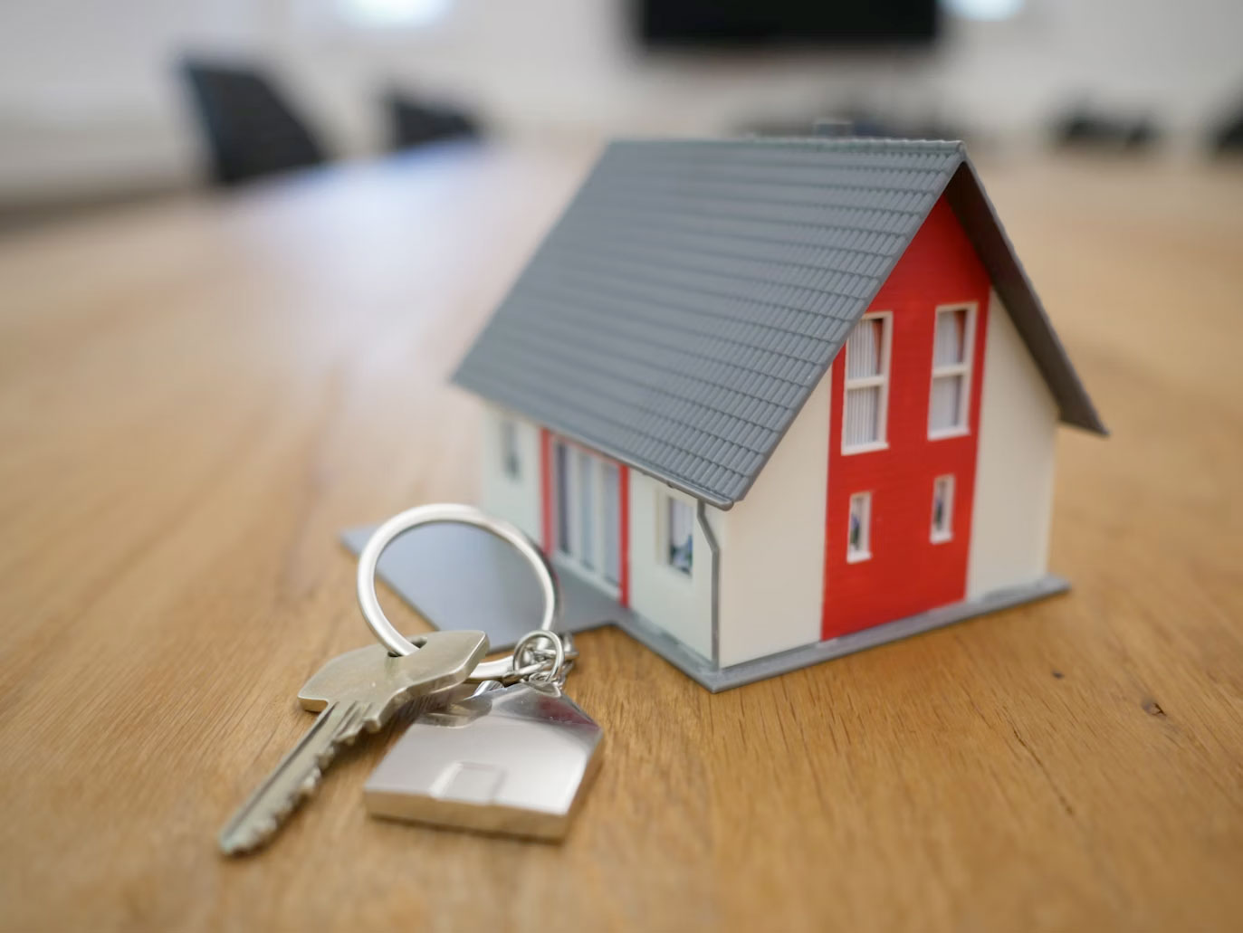 Image featuring a small model home and car keys in foreground.